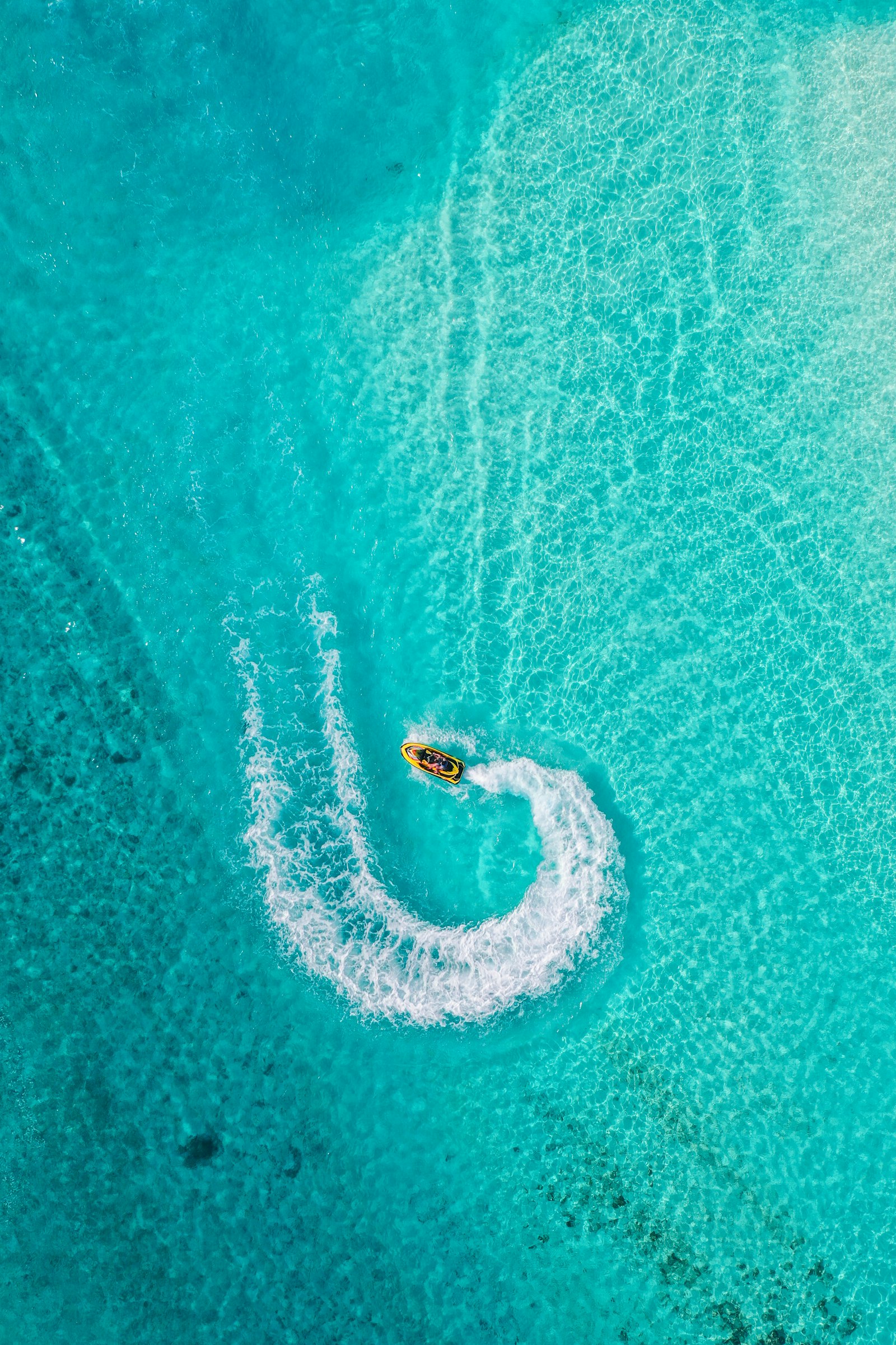 Aerial view of a jet ski carving a circle in turquoise shallows